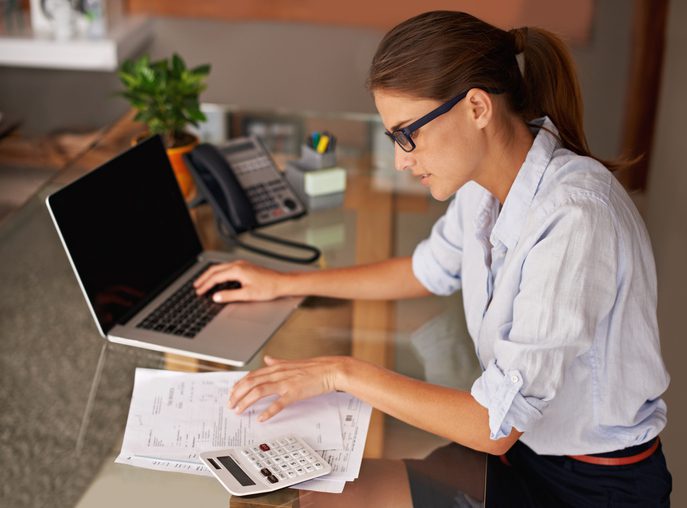 Martinson & Carter, CPAs, PA | woman in a white shirt and wearing glasses sitting at her desk typing information into her laptop while going over tax records