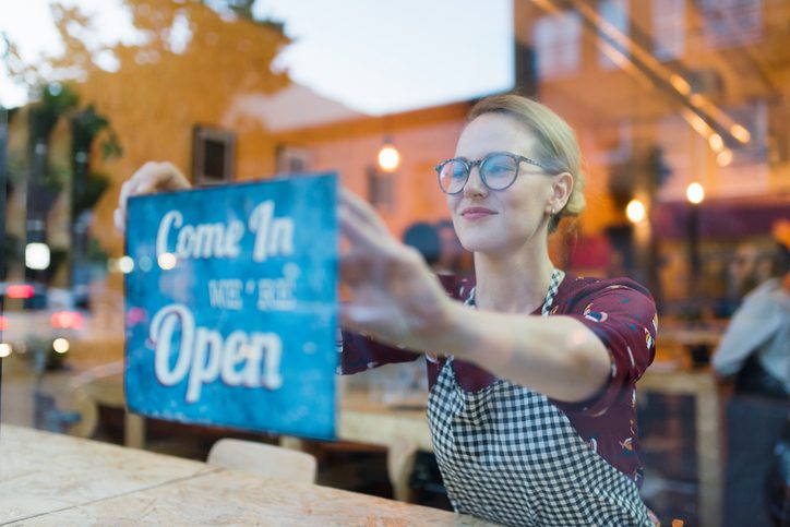 Martinson & Carter, CPAs, PA | blonde haired woman with glasses smiling as she puts up an Open sign on the window of your store